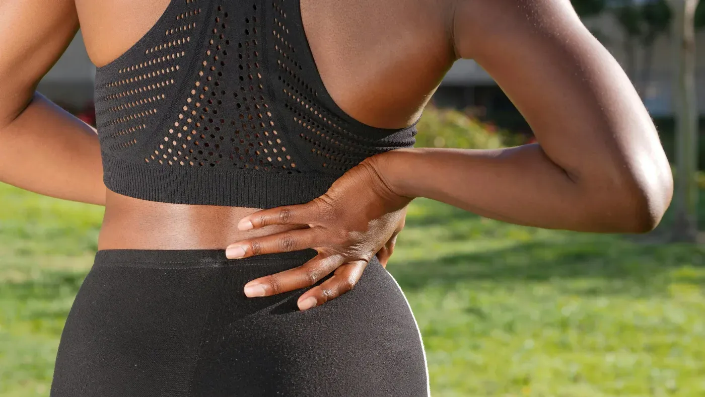 A person outdoors pressing both hands into their lower back