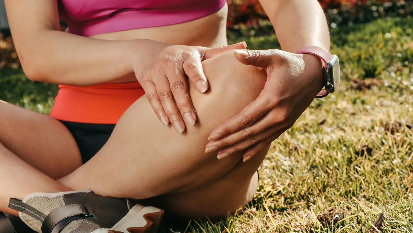 A woman seated on the grass holding her knee with both hands