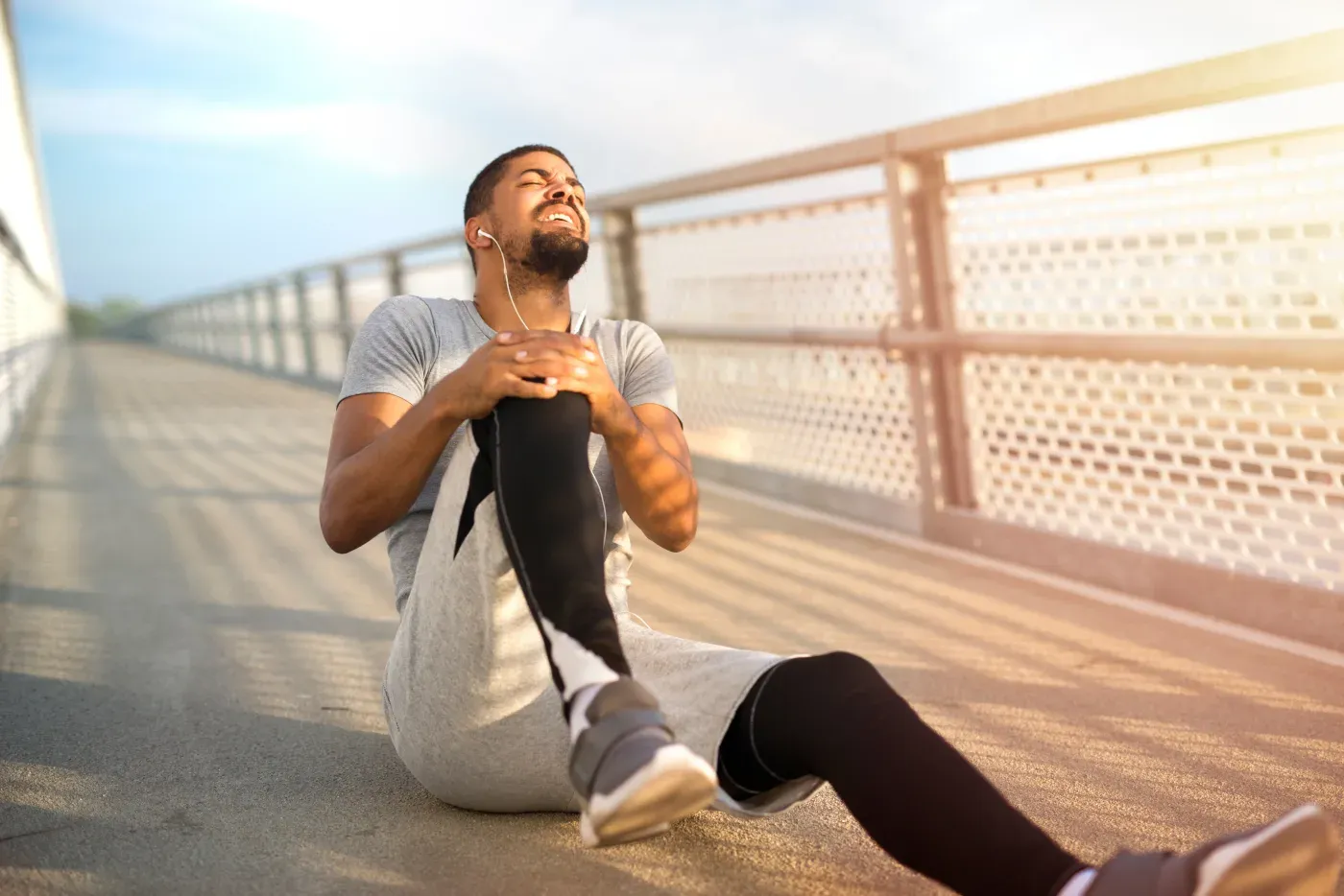 A man sitting on a footbridge holding his lower leg after a run