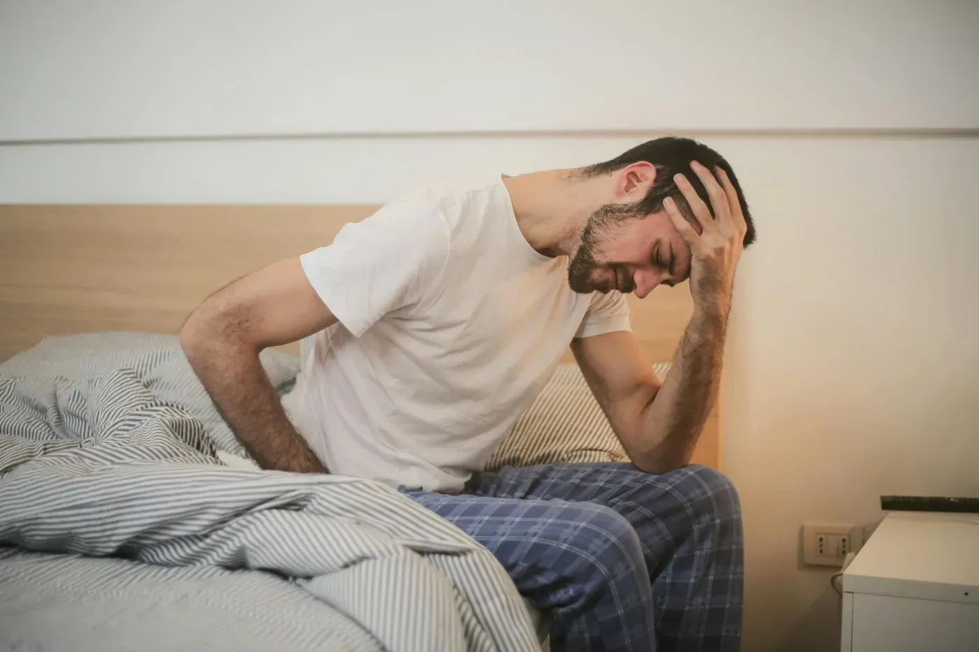 A man sitting on the edge of a bed holding the back of his neck